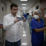 Vereador dentro de hospital filmando as dependências internas com uma enfermeira ao seu lado.