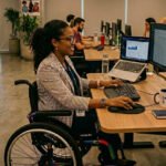 Pessoa com deficiência física em cadeira de rodas usando computador em ambiente de trabalho acessível