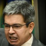 Senador Randolfe Rodrigues com bandeiras do Amapá e do Senado Federal ao fundo