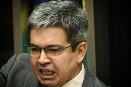 Senador Randolfe Rodrigues com bandeiras do Amapá e do Senado Federal ao fundo